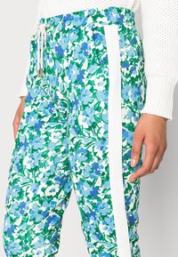 Květinové kalhoty se zeleným, modrým a bílým vzorem; mají stahovací pas a bílé postranní pruhy; měkká textura.