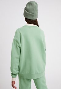 Sweat-shirt vert surdimensionné en tissu doux, avec un col arrondi et des poignets côtelés. Associé à un pantalon assorti et un bonnet vert.