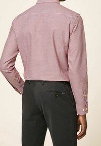 Czerwona i biała koszula w kratę z długimi rękawami, kołnierzykiem zapinanym na guziki i mankietami; w połączeniu z ciemnymi spodniami z tylną kieszenią na guzik.