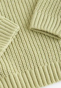 Pull en tricot vert clair avec des poignets et un ourlet côtelés épais, présentant un motif de point texturé détaillé sur un tissu doux.