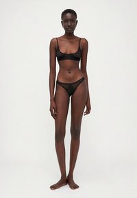 Musta pitsiset alusvaatesetti, jossa on ohuet olkaimet omaava bralette ja siihen sopiva läpikuultava t-panta. Yksityiskohtainen kukkakuvio ja aaltoilevat reunat.