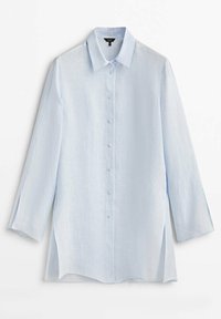 Chemise bleu clair à manches longues avec col et fentes latérales, présentée sur fond blanc.