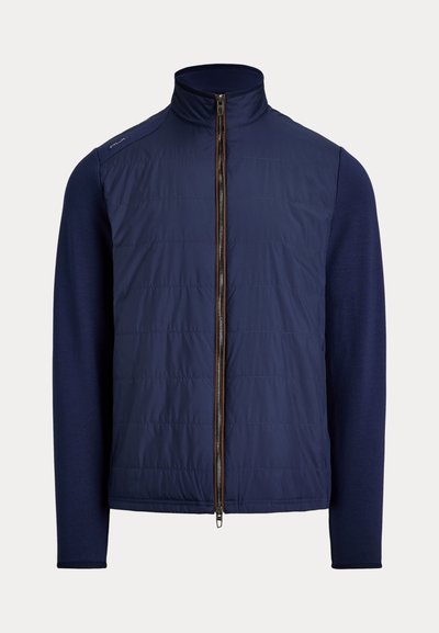 Chaqueta híbrida azul marino con parte delantera acolchada, mangas largas de punto, cuello perkins y cremallera frontal completa.