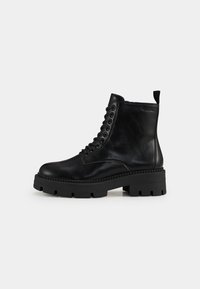 Bottines en cuir noir avec une semelle en caoutchouc épaisse, design à lacets et une languette à l'arrière pour un enfilage facile. Texture lisse.