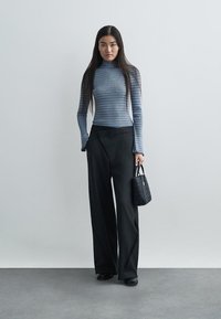 Un col roulé ajusté à rayures bleues à manches longues associé à un pantalon large à fines rayures noires, complété par un petit sac à main noir.