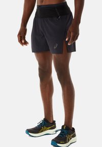 Zwarte lichtgewicht hardloopshorts met een mesh tailleband, zijsplits voor mobiliteit en een reflecterend logo. Gecombineerd met zwart-blauwe hardloopschoenen.