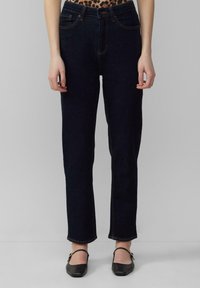 Granatowe dżinsy o prostym kroju, z pomarańczowymi przeszyciami, szlufkami na pasek i kieszeniami z przodu. Nosi je w połączeniu z czarnymi balerinami.