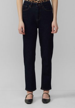 Donkerblauwe denim jeans met een rechte pasvorm, voorzien van oranje stiksels, riemlussen en zijzakken. Draagt met zwarte ballerina's.