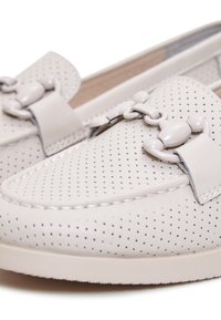 Mocassins en cuir blanc perforé avec un détail décoratif de boucle liée à l'avant et une couture blanche visible.