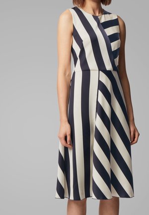 Mouwloze jurk tot op de knie met afwisselend brede zwarte en witte verticale en diagonale strepen op het bovenlijf en de rok.