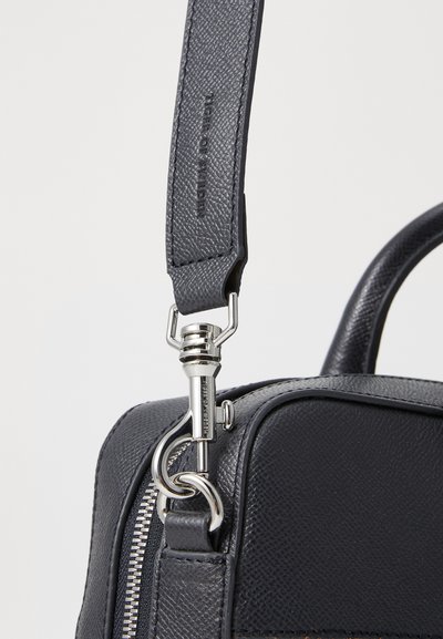 Sac en cuir gris foncé avec une finition texturée, matériel en argent, bandoulière amovible et fermeture éclair pour un accès sécurisé.