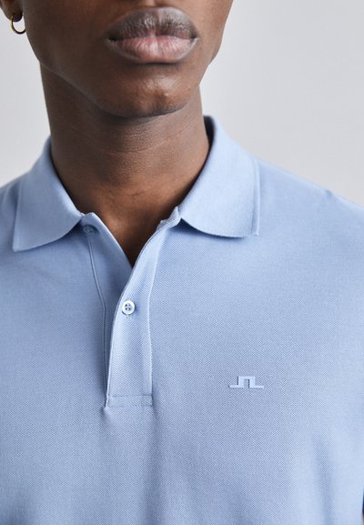Light blue polo shirt made from textured fabric, featuring a three-button placket and a small, subtle logo on the chest.