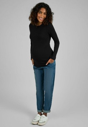 Haut noir à manches longues, en tissu doux, design ajusté, associé à un jean bleu ample, retroussé à la cheville, et des baskets blanches.