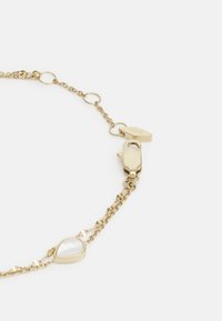 Pulsera de cadena en tono dorado con un acento de perla en forma de corazón. Presenta un cierre de langosta y eslabones, exhibiendo un diseño elegante y pulido.