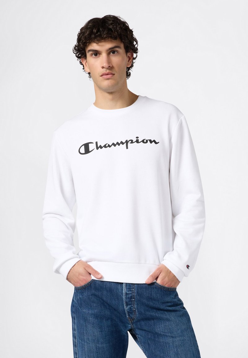 Sweat-shirt blanc en coton avec un col rond et des manches longues. Présente un logo "Champion" noir bien en vue sur la poitrine.