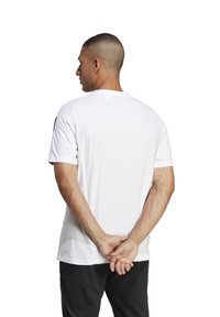 T-shirt sportif blanc à manches courtes avec une texture lisse et un col rond, montré de dos, associé à un pantalon noir.