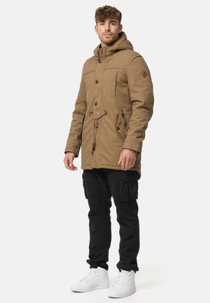 Bruine parka met een taillekoord, knoopsluitingen en zakken. Gecombineerd met zwarte cargobroek en witte sneakers.