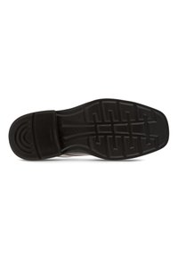 Black rubber shoe sole with textured tread for grip, featuring a raised circular design at the heel and a smooth finish at the toe.