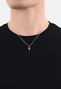 Goldener Kreuzanhänger an einer feinen Kette, getragen über einem schwarzen T-Shirt. Die Kette hat ein zartes Design mit einem subtilen Glanz.