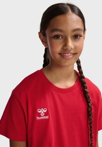 Rød bomulds T-shirt med rund hals og korte ærmer. Har hvidt broderet logo på venstre brystområde. Glat tekstur.