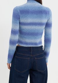 Tajta, långärmad tröja i gradientnyanser av blått, med hög krage och mjukt, strukturerat tyg. Kombineras med mörka jeans.