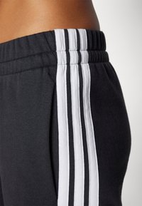Czarne sportowe spodnie z miękkiej tkaniny, z trzema białymi pionowymi paskami po bokach oraz elastycznym ściągaczem w talii dla zapewnienia komfortu.