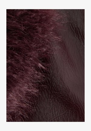 Pluche bordeauxroze bont aan de linkerkant gaat over in een glad, glanzend bruin oppervlak met een fijne, verticale textuur aan de rechterkant.