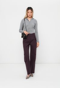 Grå zip-up kort tröja med flätad struktur, tillsammans med mörk lila vida cargobyxor med sidofickor och en stilren svart väska.