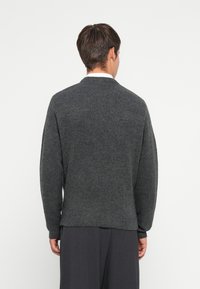 Grijze gebreide trui met een ronde hals, verlaagde schouders en ribgebreide manchetten. De stof heeft een zachte textuur en het ontwerp is simpel en modern.