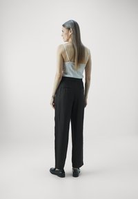 Zwarte op maat gemaakte broek met een hoge taille, achterzakken en een soepele textuur; gedragen met een witte lichte tanktop en zwarte schoenen.