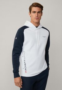 Biela a námornícka kapucňová mikina s predným klokankovým vreckom. Obsahuje logo potlačené na boku a kontrastné raglánové rukávy.