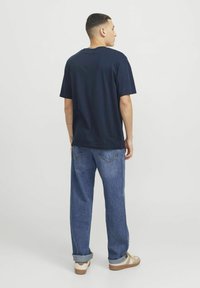 Tumesinine puuvillane T-särk lühikeste varrukatega, mille on paaritatud heledate denimitega, mis on lõdva istuvusega ja mansettidega, ning kantud heledate tossega.