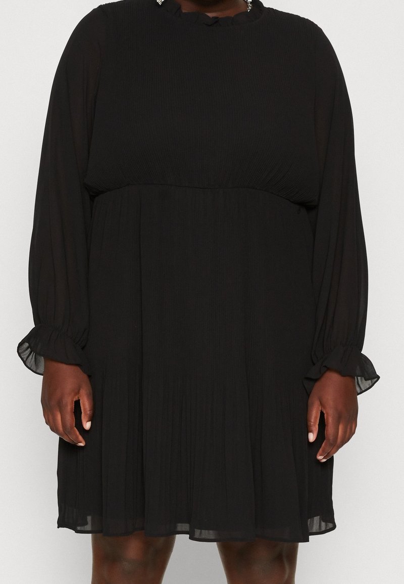 Robe noire plissée à manches longues, avec un col à volants et des poignets élastiques, offrant une coupe ample et un tissu léger et transparent.