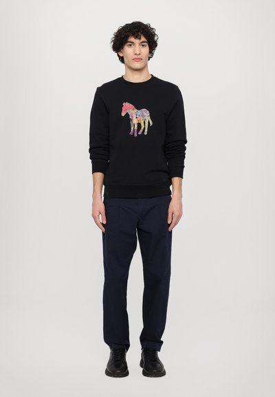 Black sweatshirt featuring a colorful horse graphic, paired with dark navy pants and black shoes. Simple round neck and ribbed cuffs.