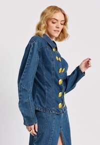 Denim jakna u srednje plavoj boji s uskim dizajnom, s velikim zlatnim dugmadima, strukturiranim ovratnikom i detaljima na šavovima. Dugi rukavi.
