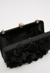 Pochette in tessuto nero con fiori decorativi in tessuto nero sulla parte anteriore e chiusura a scatto in tono oro, mostrata aperta.
