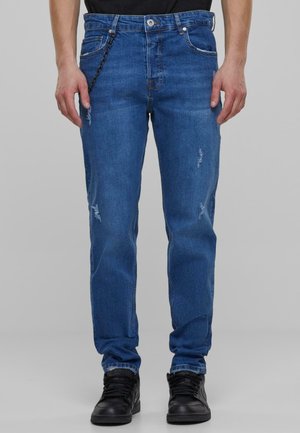 Blå denim jeans med rett passform, slitte detaljer og en kjedeakens på midjen. Kombinert med svarte sneakers.