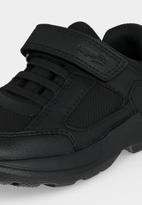 Chaussure de sport noire en tissu texturé, lacets élastiques et bride velcro étiquetée "superfit" sur fond blanc.