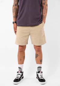 Shorts en velours côtelé beige avec poches avant, coupe droite et tissu texturé ; associés à des baskets montantes noires et des chaussettes blanches à motifs.