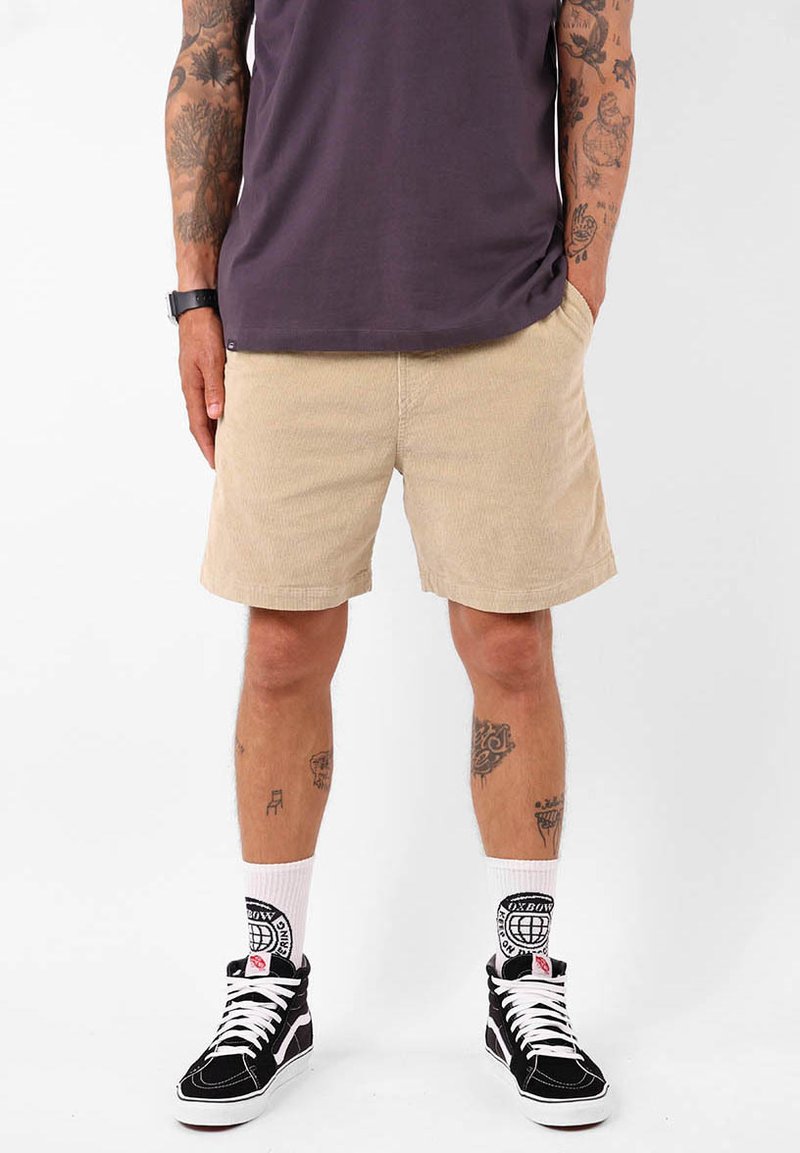 Shorts en velours côtelé beige avec poches avant, coupe droite et tissu texturé ; associés à des baskets montantes noires et des chaussettes blanches à motifs.