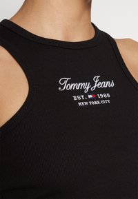 Gros plan d'un débardeur noir côtelé avec le texte blanc "Tommy Jeans EST. 1985 NEW YORK CITY" et une petite broderie logo rouge, blanc et bleu.