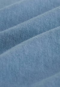 Baumwollstoff in einem hellblauen Farbton, mit einer glatten Textur und einem subtilen Webmuster, in sanften, überlappenden Falten angeordnet.