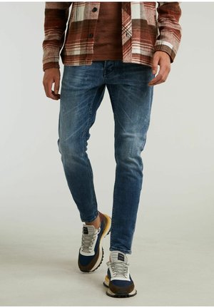Jeans de mezclilla azul claro con un corte ajustado, que presentan una textura desgastada. Combinados con zapatillas de color bloque en azul, marrón y gris.