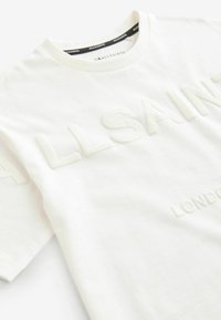 Bílý bavlněný tričko s vyraženým nápisem "ALLSAINTS LONDON" v světlé barvě, kulatý výstřih, krátké rukávy a hladká textura.
