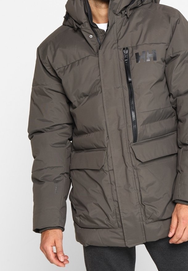 Giacca a vento in grigio scuro. Presenta una tasca sul petto con zip, due tasche frontali, un cappuccio e un design a pannelli cuciti. Materiale liscio e resistente all'acqua.