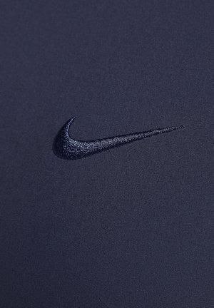Marine sportsstof har et broderet Nike-logo i en mørkere nuance, glat tekstur og nærbillede, der fremhæver materialets kvalitet.