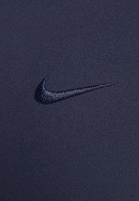 Marinblå atletisk tyg med en jämn struktur, med en broderad svart Nike swoosh-logotyp. Närbild som betonar detaljer.
