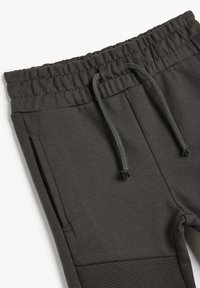 Dunkelgraue Jogginghose aus weichem Stoff mit elastischem Bund und Kordelzug. Verfügt über seitliche Taschen und strukturierte Knieakzente.