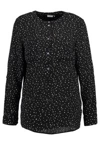 Blusa nera a maniche lunghe con motivo a stelle e pois bianchi, scollatura rotonda, chiusura anteriore con bottoni di colore viola e due taschini sul petto.