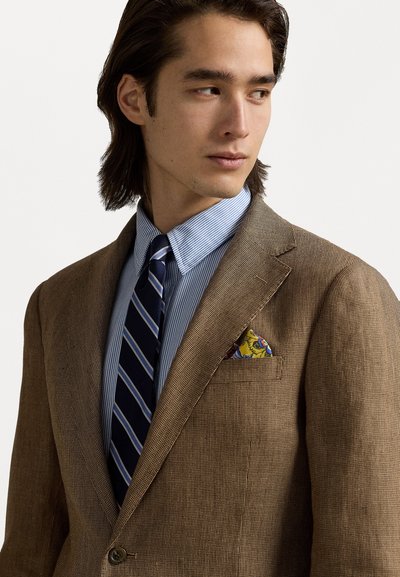 Bruine textuur blazer over een lichtblauw gestreept overhemd, met een donker gestreepte stropdas en een gemêleerde pochet met gele en blauwe accenten.